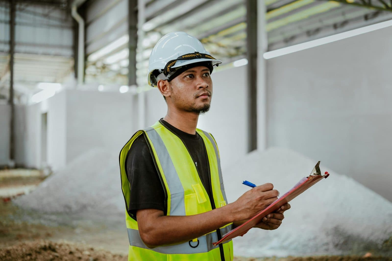 A site supervisor in a hard hat and high-visibility vest taking notes