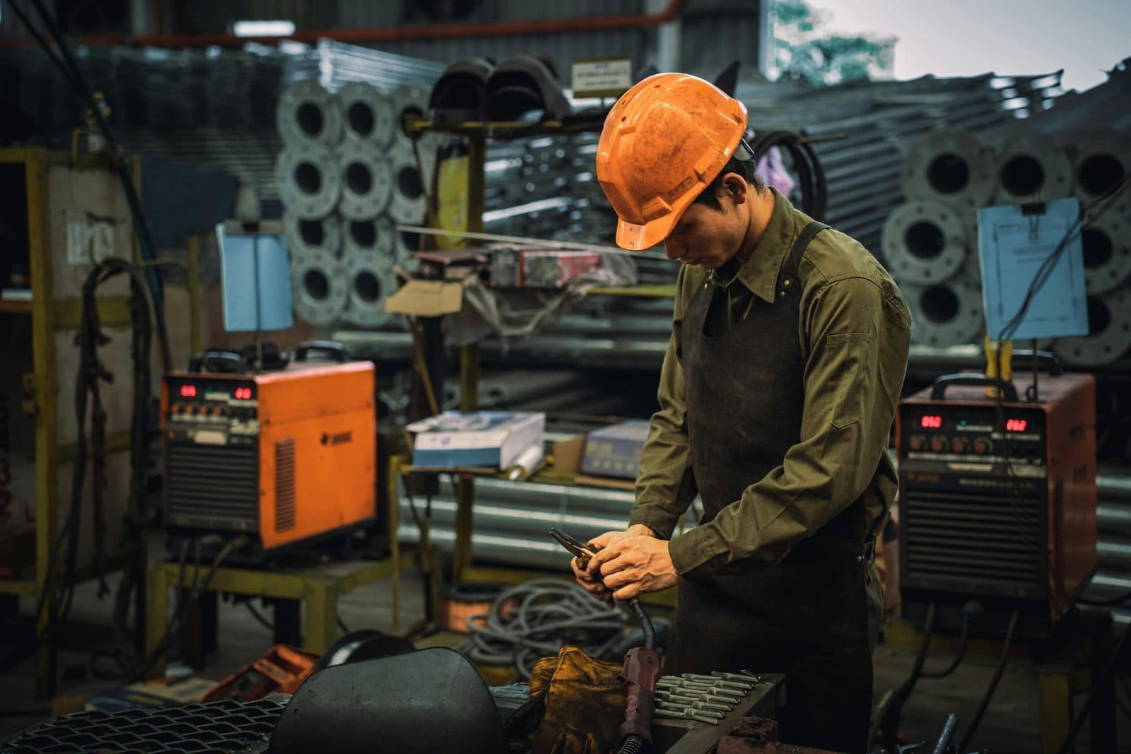 A tradesman in an orange hard hat working at a bench in a workshop