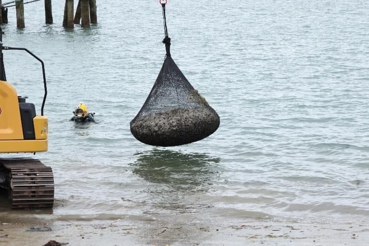 An excavator placing a rock bag in shallow water