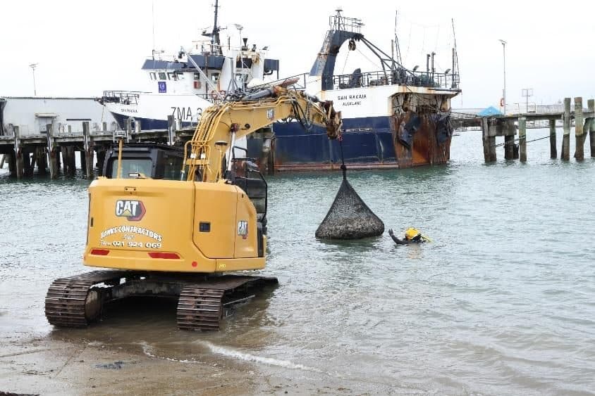 An excavator placing a rock bag in the water at a port